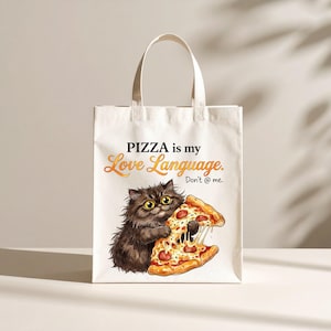 May include: A white tote bag featuring a graphic of a fluffy dark brown cat holding a slice of pepperoni pizza. The text reads PIZZA is my Love Language. Don't @ me. The bag has two top handles and a rectangular shape with a clean, flat design.