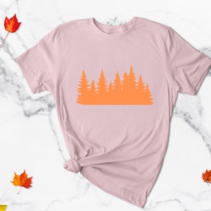 May include: A pink t-shirt with an orange silhouette of a forest on the front.
