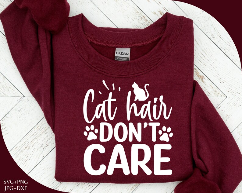 Może przedstawiać: Bordowy sweter z białym napisem "Cat hair don't care" z odciskiem łapy po obu stronach słowa "don't".