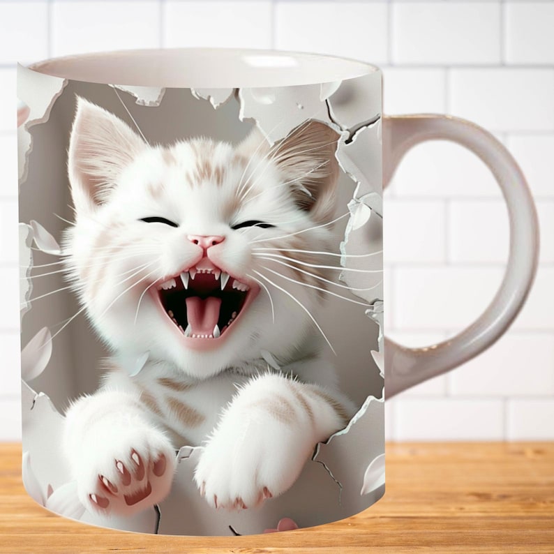 Pu&ograve; includere: Tazza in ceramica bianca con un'immagine 3D di un gattino bianco con macchie marroni che spunta da un buco nella tazza. Il gattino ha la bocca aperta e ride.