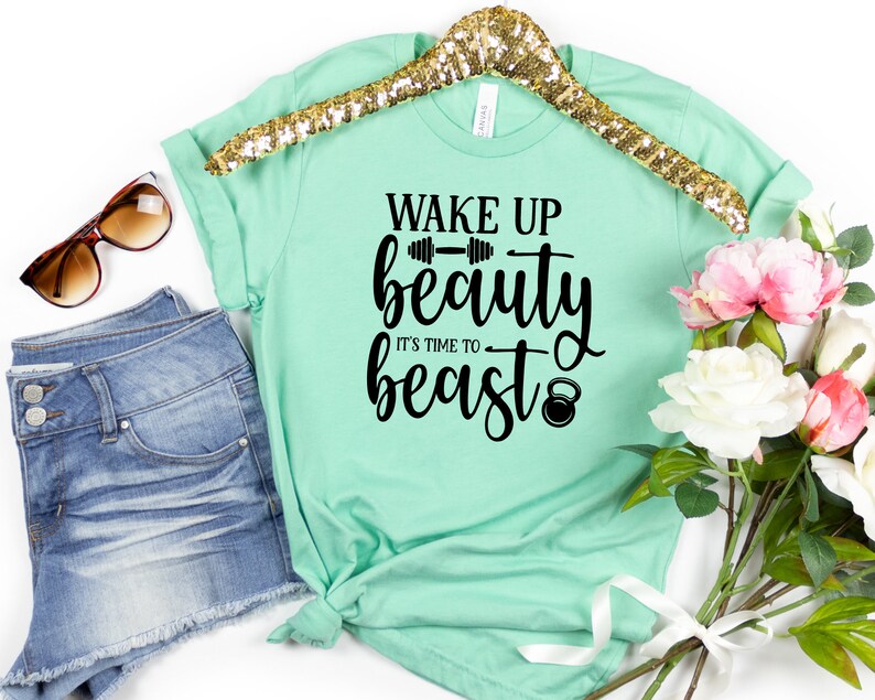 Op de afbeelding: Een mintgroen T-shirt met de tekst "Wake Up Beauty It's Time To Beast" in zwarte letters. De tekst bevat een halter en een kettlebell.