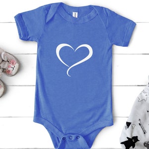 May include: A blue baby onesie with a white heart design. The onesie is on a white wooden surface.