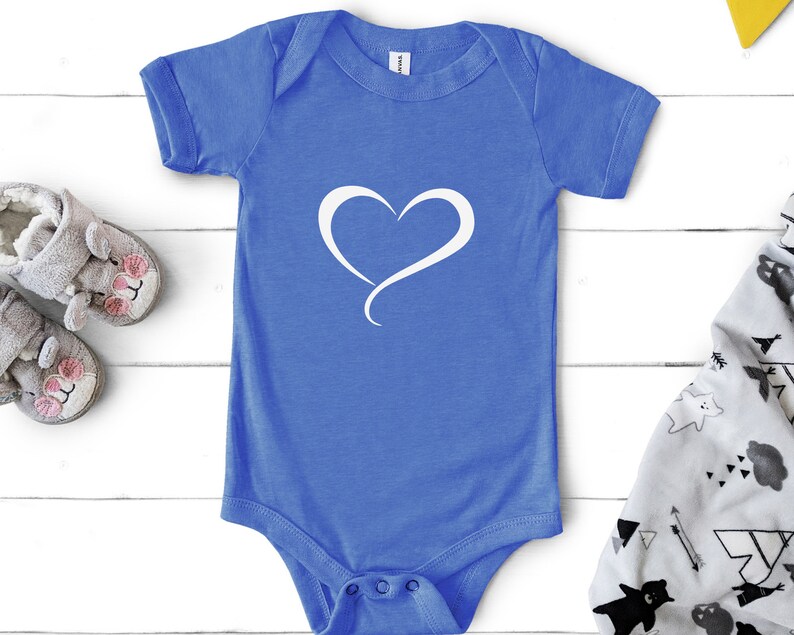 May include: A blue baby onesie with a white heart design. The onesie is on a white wooden surface.