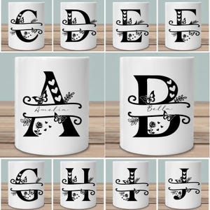 Op de afbeelding: Witte keramische mokken met zwarte monogramletters, versierd met vlinders, harten en bloemmotieven. De mokken tonen de letters C, D, E, F, A, B, G, H, I en J. Sommige mokken hebben namen erop geschreven.