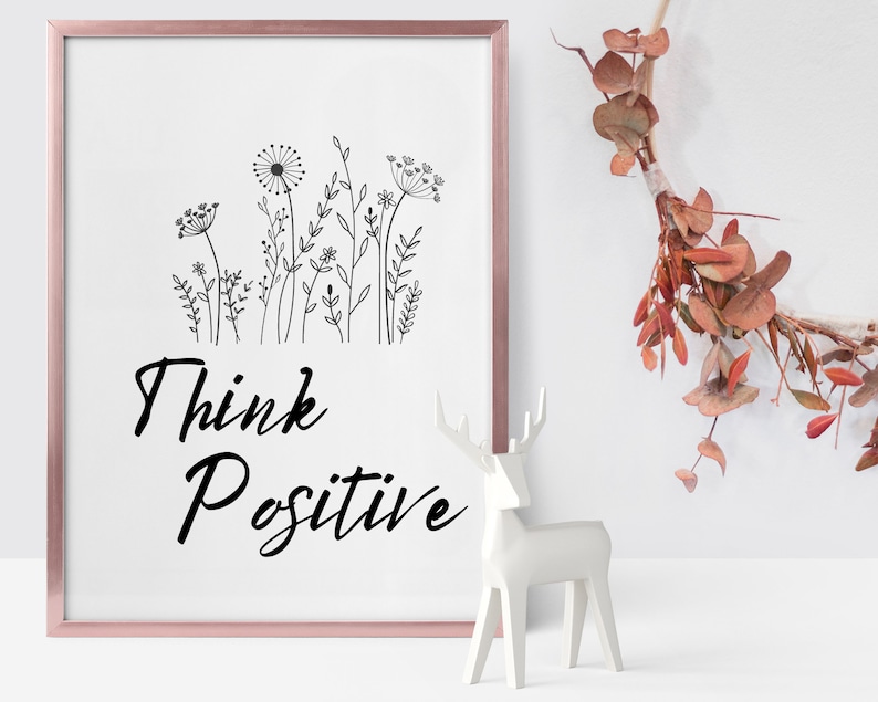 May include: A framed print with a black and white illustration of wildflowers and the text "Think Positive". A white ceramic deer figurine is in the foreground.