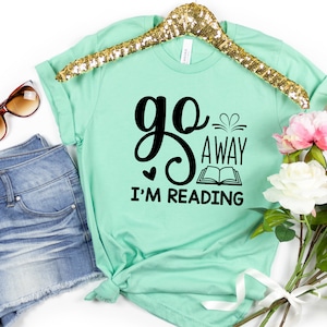 May include: A light green t-shirt with black text that reads "go away i'm reading" with a book graphic and hearts.