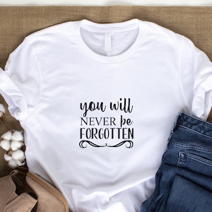 May include: White t-shirt with black text that reads "you will never be forgotten".