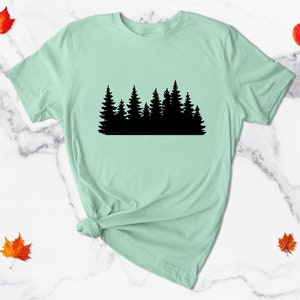 May include: A light green t-shirt with a black silhouette of a forest on the front.