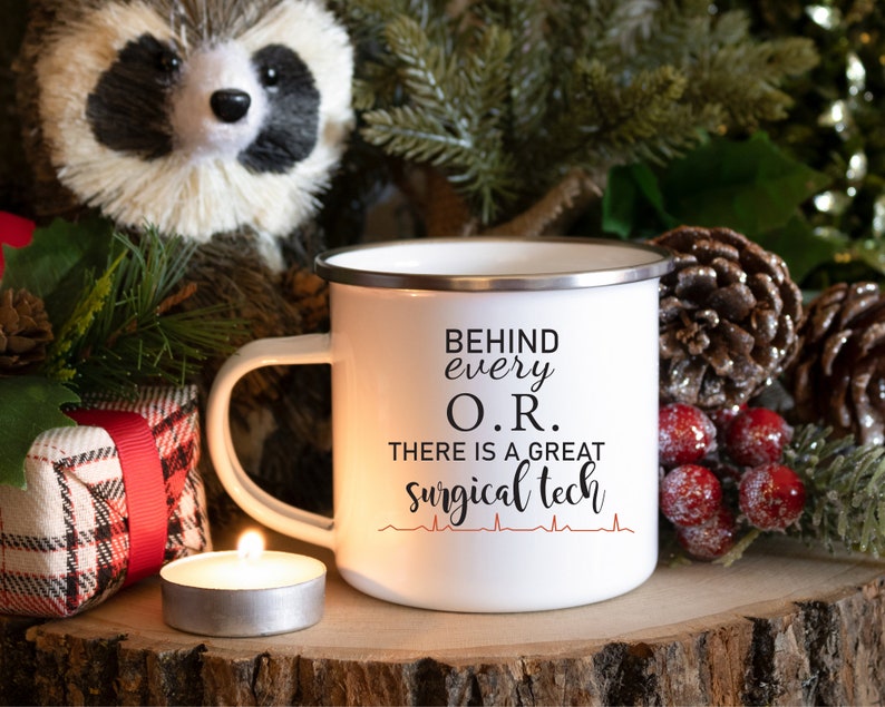 May include: White enamel mug with a black and red design. The mug says "Behind every O.R. there is a great surgical tech" with a red heartbeat graphic.