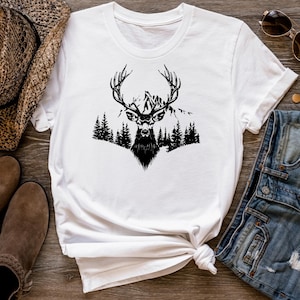 May include: White t-shirt with a black silhouette of a deer with antlers standing in front of a mountain range and trees.