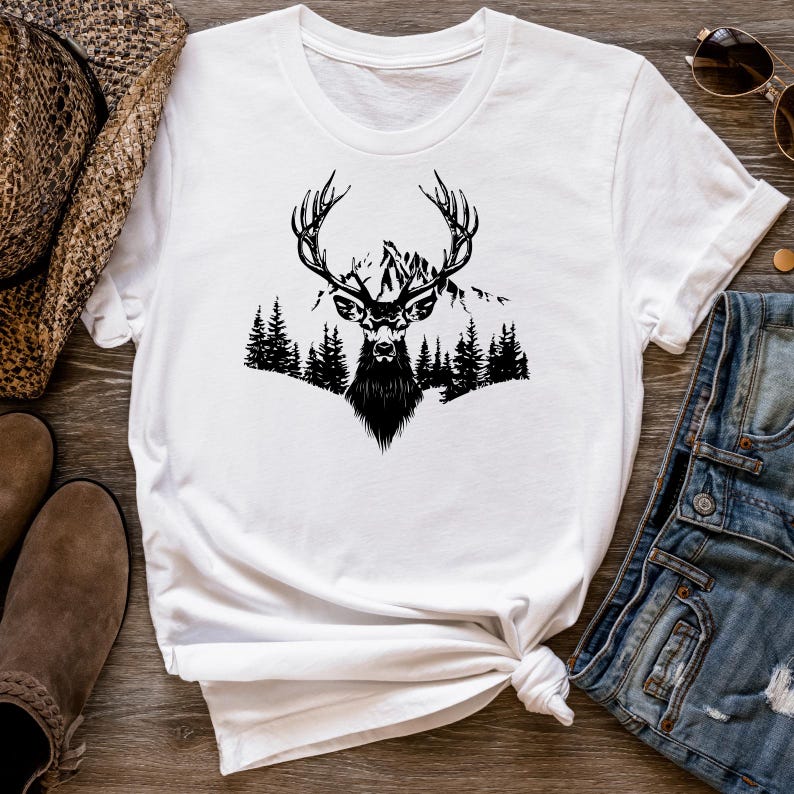 May include: White t-shirt with a black silhouette of a deer with antlers standing in front of a mountain range and trees.