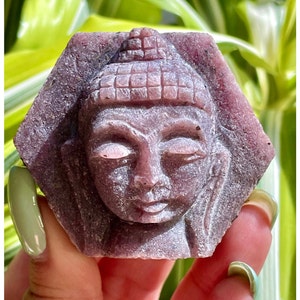Pu&ograve; includere: Una statua di Buddha scolpita in una pietra preziosa viola con un viso dettagliato e una testa testurizzata.