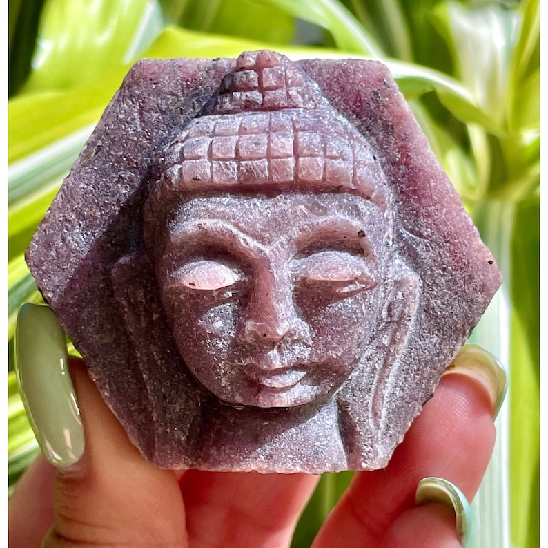 Pu&ograve; includere: Una statua di Buddha scolpita in una pietra preziosa viola con un viso dettagliato e una testa testurizzata.