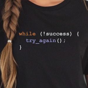 May include: Black t-shirt with white text that reads "while (!success) { try_again(); }"