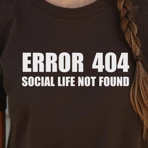 Peut inclure: Un t-shirt marron avec un texte blanc qui dit "ERROR 404 SOCIAL LIFE NOT FOUND".