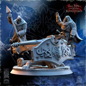 May include: A gray plastic miniature wargaming model of a siege weapon with two figures. The weapon is a large cannon with a shield-shaped front and a wolf's head design. One figure is standing on the cannon, holding a sword and shield. The other figure is kneeling on the ground, holding a spear. The text "One Sin for Seven Kingdoms" is visible in the background.