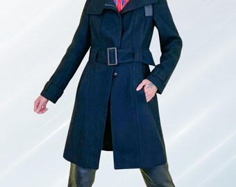 May include: A black wool coat with a wide collar, belted waist, and a single button closure. The coat features a belt with a rectangular buckle and a small leather accent on the shoulder. The coat has long sleeves and pockets.