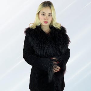 May include: A black suede coat with a fluffy, textured collar and cuffs. The coat has a classic design and appears to be made of high-quality materials. The model is wearing the coat, showcasing its fit and style.