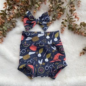 May include: A navy blue baby bloomer with a whimsical print of glasses, wands, feathers, and the number "9 3/4". A matching navy blue and pink bow is included.
