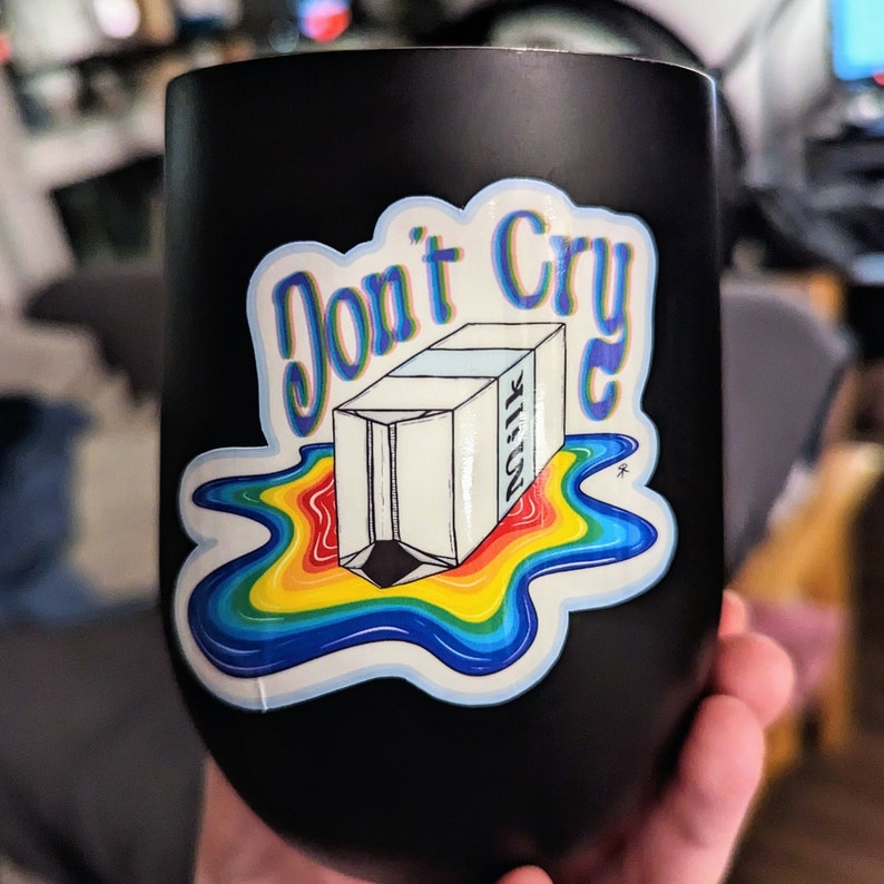 May include: Black insulated tumbler with a sticker that reads "Don't Cry" above a carton of milk. The milk carton is spilling a rainbow of colors.