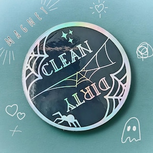 Puede incluir: Un im&aacute;n redondo y hologr&aacute;fico con las palabras "CLEAN" y "DIRTY" en blanco, con un dise&ntilde;o de telara&ntilde;a. La palabra "MAGNET" est&aacute; escrita a lo largo del borde superior. Tambi&eacute;n se ve una ara&ntilde;a y estrellas.