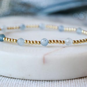 May include: A delicate bracelet made with small gold beads and light blue gemstone beads.