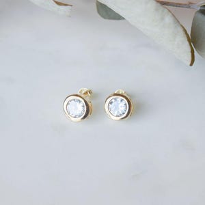 May include: A pair of gold stud earrings with a clear round stone in the center of each earring.