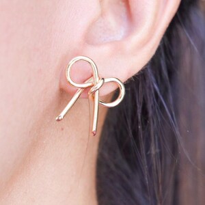 May include: Gold bow-shaped earrings. The earrings are made of a thin, twisted wire and are designed to look like a bow.