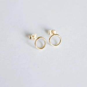 May include: A pair of gold circle stud earrings. The earrings are simple and minimalist, with a smooth, polished finish.
