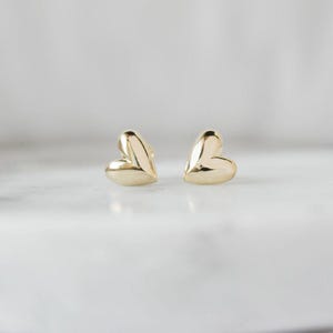 May include: A pair of small, gold heart-shaped stud earrings.