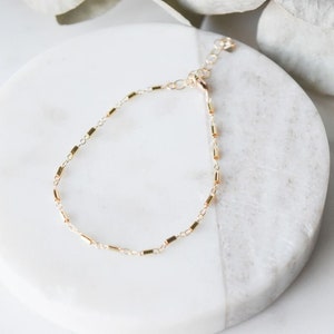 May include: A delicate gold chain bracelet with a simple, minimalist design. The bracelet is made of small, rectangular links and has a lobster clasp closure.