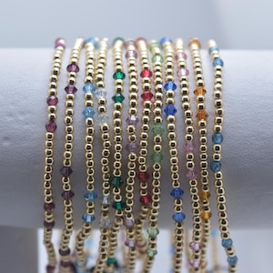May include: A collection of beaded bracelets with gold-colored beads and colorful crystal accents. The bracelets are displayed vertically, showcasing a variety of colors including purple, blue, green, and red.