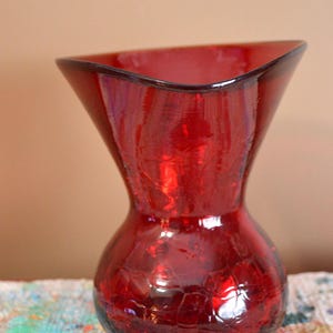 May include: A red glass vase with a crackle finish. The vase has a flared top and a rounded base. The vase is approximately 8 inches tall.