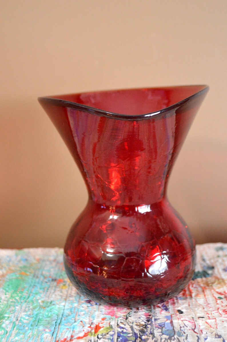 May include: A red glass vase with a crackle finish. The vase has a flared top and a rounded base. The vase is approximately 8 inches tall.