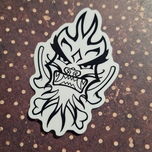 Puede incluir: Pegatina en blanco y negro de una cabeza de dragón estilizada con una expresión feroz. La cabeza del dragón está delineada en negro y tiene un fondo blanco.