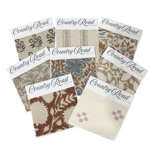 May include: A selection of fabric samples showcasing floral and patterned designs. Each sample is labelled with "Country Road TEXTILES". The fabrics display a range of colours, including beige, brown, and blue, suitable for interior design.