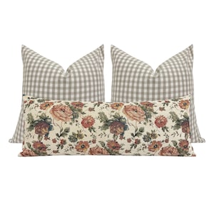 May include: Two beige gingham pillow covers with a floral patterned lumbar pillow in the center. The floral pillow has a cream background with red, orange, and green flowers.