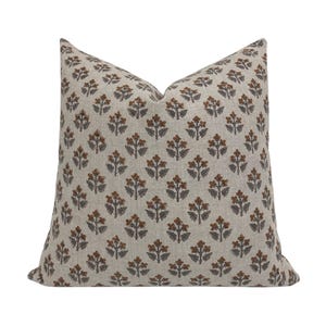 May include: A square throw pillow featuring a light beige linen-like fabric base with a repeating pattern of small, stylized floral motifs in shades of burnt orange and dark charcoal gray, arranged in a symmetrical grid across the entire surface.