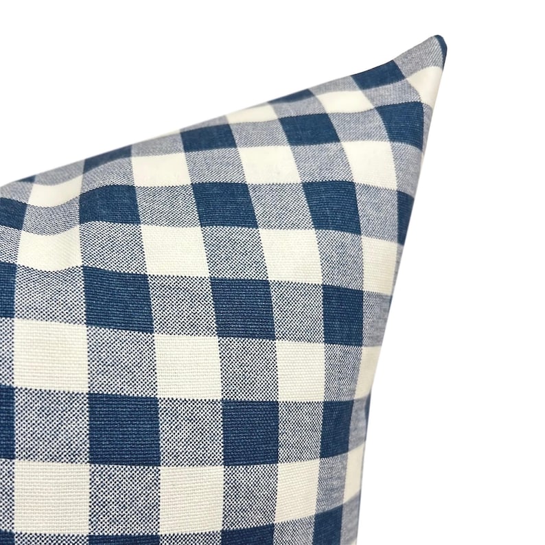 May include: Close-up of a blue and white checkered pillow. The pillow has a classic gingham pattern, with large squares of navy blue and off-white. The fabric appears to be a woven cotton or linen, with a slightly textured surface.