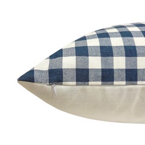 May include: A decorative pillow with a blue and white checkered pattern on the top half and a solid beige linen fabric on the bottom half. A zipper is visible on the side. The pillow is a home decor item.