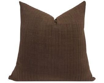 May include: A brown pillow with a textured, striped pattern. The pillow is made of a soft, woven fabric.
