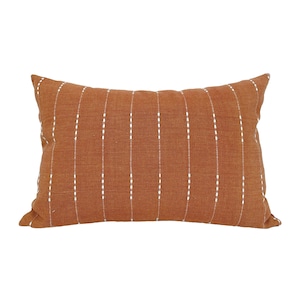 May include: A rectangular throw pillow with a rust-colored fabric and white stitching in a vertical stripe pattern.