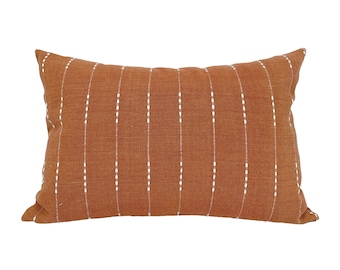 May include: A rectangular throw pillow with a rust-colored fabric and white stitching in a vertical stripe pattern.