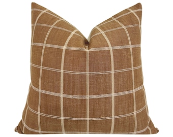 May include: A square decorative pillow with a brown plaid pattern. The pillow features a grid design with thin, off-white lines against a solid brown background. The pillow is made of a textured fabric.