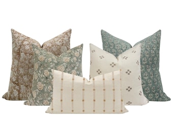 May include: A collection of decorative throw pillows in various patterns and colors. The pillows feature floral, geometric, and striped designs in shades of beige, green, and blue. The pillows are arranged in a group, showcasing their different textures and styles.