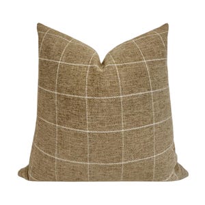 May include: A square decorative pillow with a tan fabric and a white grid pattern. The pillow has a textured appearance and is designed for home decor. The pillow is a neutral color and can be used in a variety of settings.