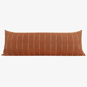 May include: A long, rectangular, rust-colored pillow with white vertical stripes. The stripes are made of small white dots.