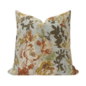 Könnte beinhalten: Quadratisches Zierkissen mit floralem Muster. Das Kissen hat einen hellblauen Hintergrund mit einem sich wiederholenden Muster aus großen Blumen in Creme-, Orange-, Braun- und Grüntönen. Das Kissen hat eine quadratische Form.