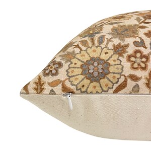 May include: A beige throw pillow with a floral pattern in shades of brown, yellow, and gray. The pillow has a zipper closure.