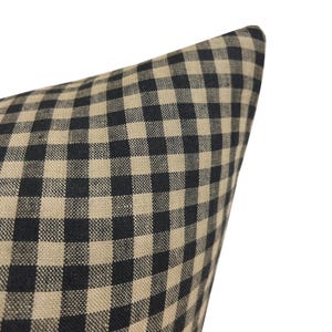 K&ouml;nnte beinhalten: Ein schwarzer und beigefarbener Gingham-Kissenbezug. Der Kissenbezug ist aus einem weichen, gewebten Stoff mit einem karierten Muster.